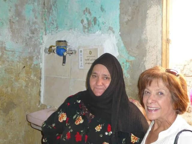 A resident and a club member beside a newly fitted water meter and tap, with the club’s Arabic donation plaque