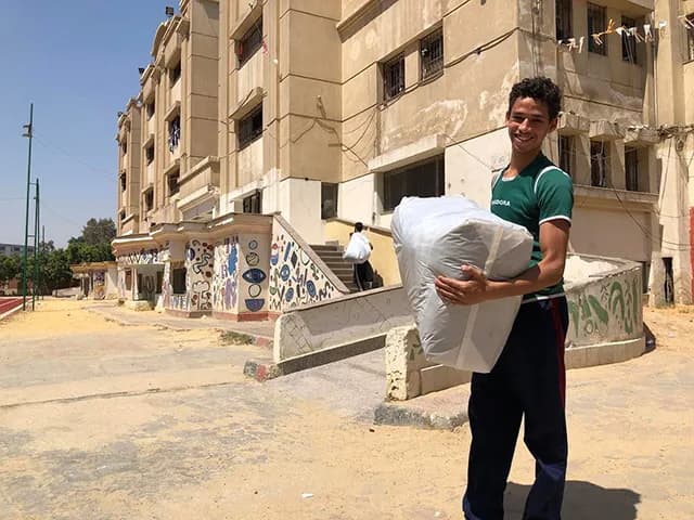 A young man carrying a large bundle of donated goods outside the Awlady Orphanage building